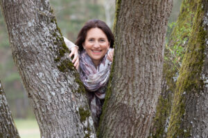 Gisela Jung lächelt, während sie zwischen zwei Bäumen hindurchschaut